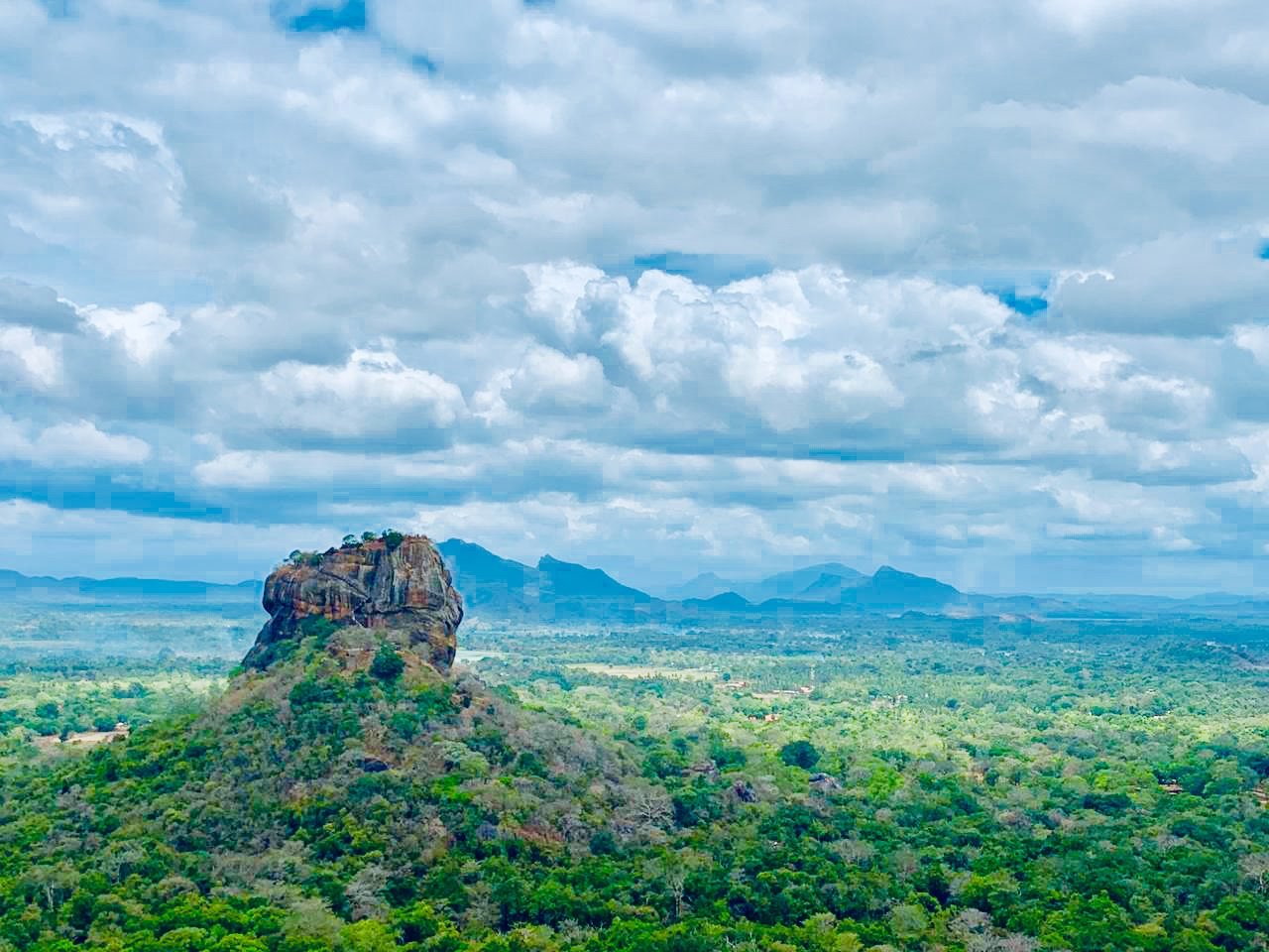 Sigiriya rock rising above the forest under a cloudy sky