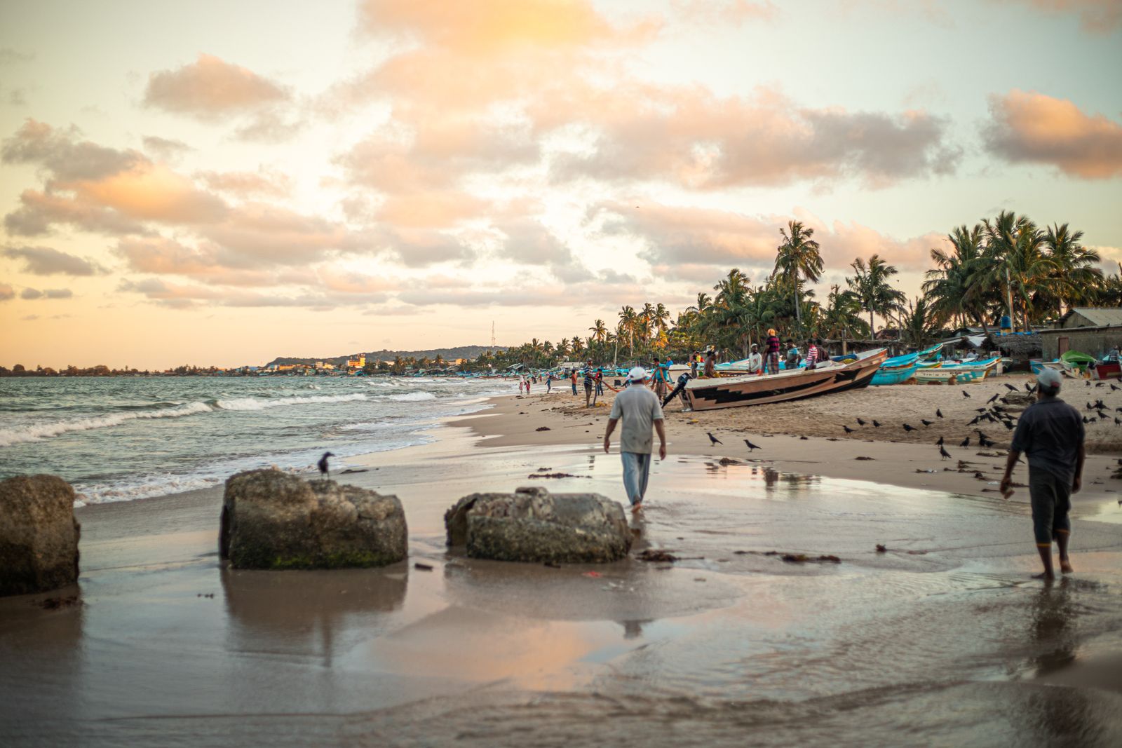 Scenic view of Trincomalee beach at sunset featuring fishermen, boats, and palm trees, Sri Lanka.