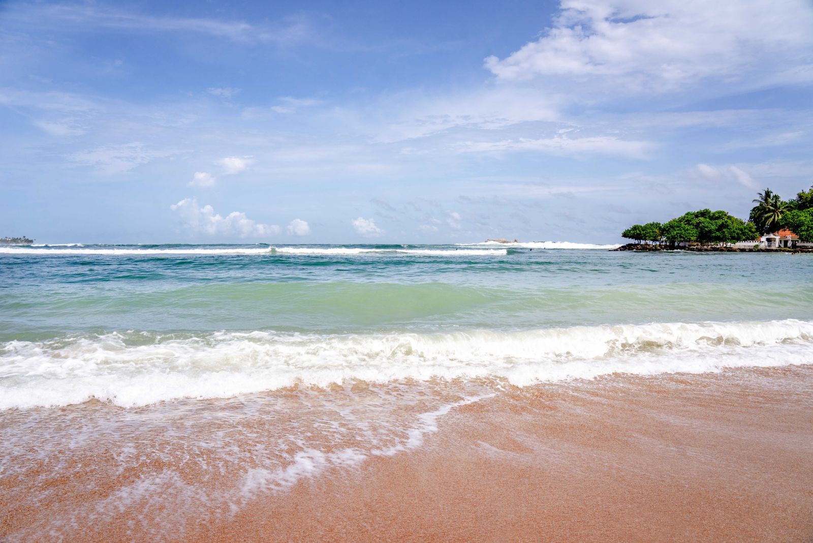 Serene view of Weligama Beach with waves gently hitting the shore under a bright sky.